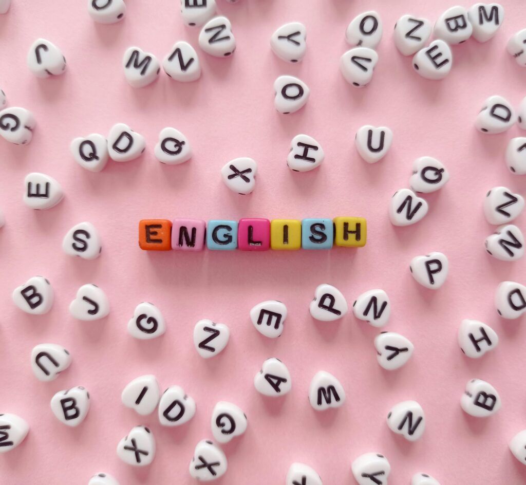 Scattered letter beads form the word 'English' on a pink background, symbolizing language learning.