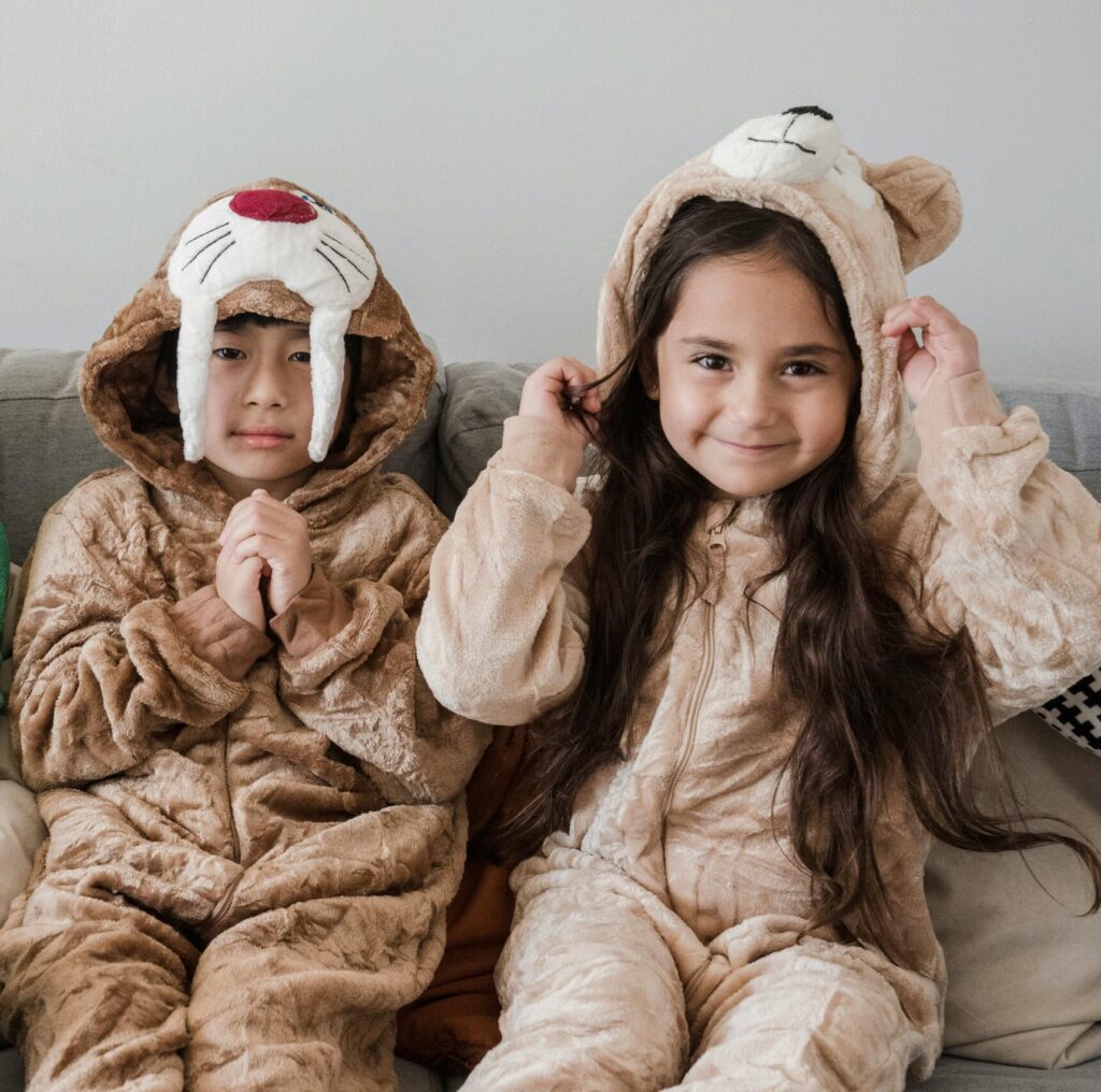 Three children in playful animal costumes smiling while sitting indoors on a sofa.