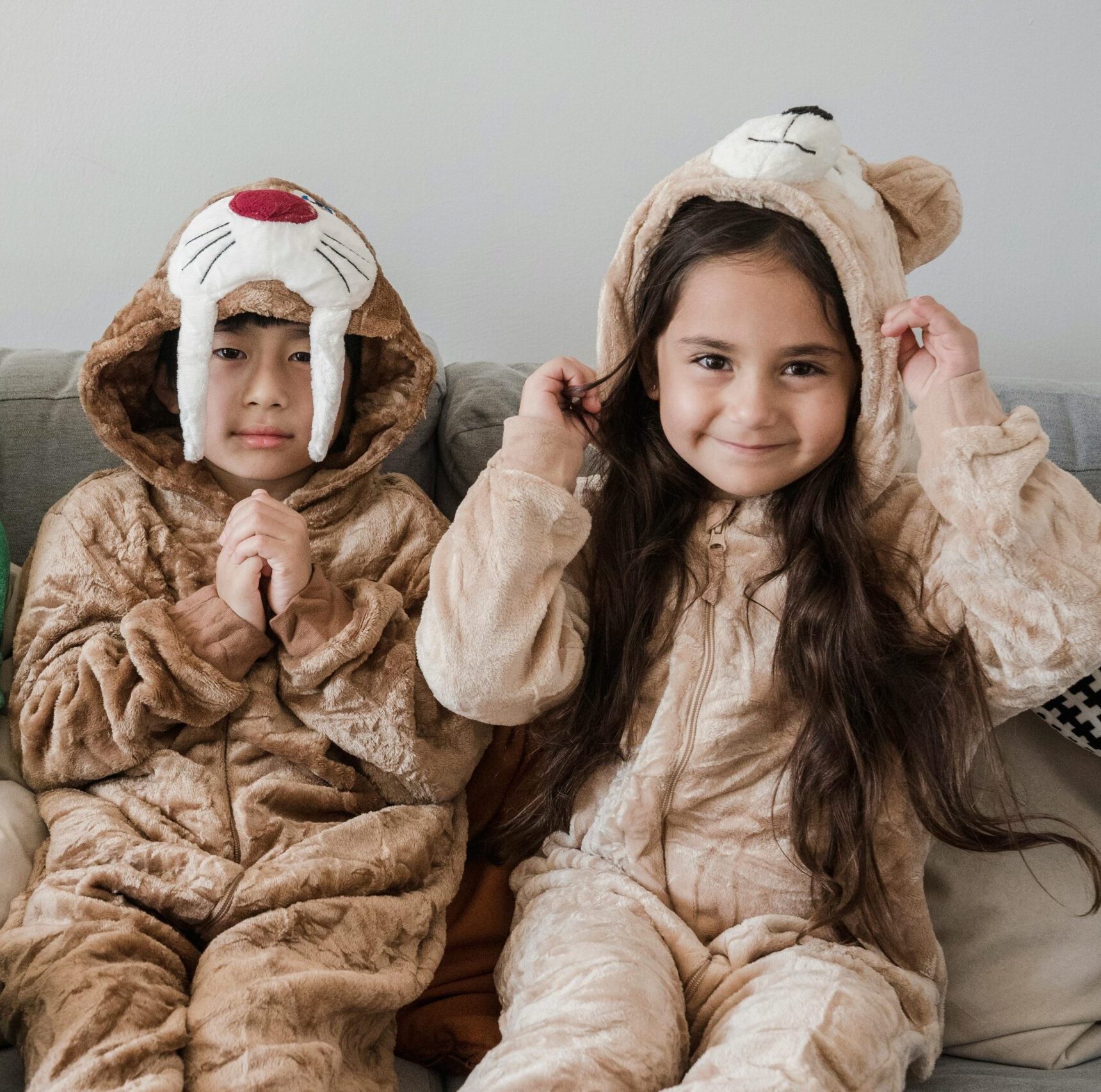 Three children in playful animal costumes smiling while sitting indoors on a sofa.